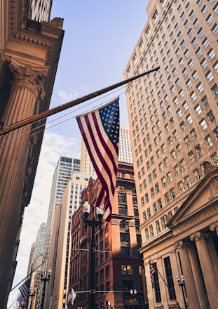 American flag hangs between tall buildings in city.