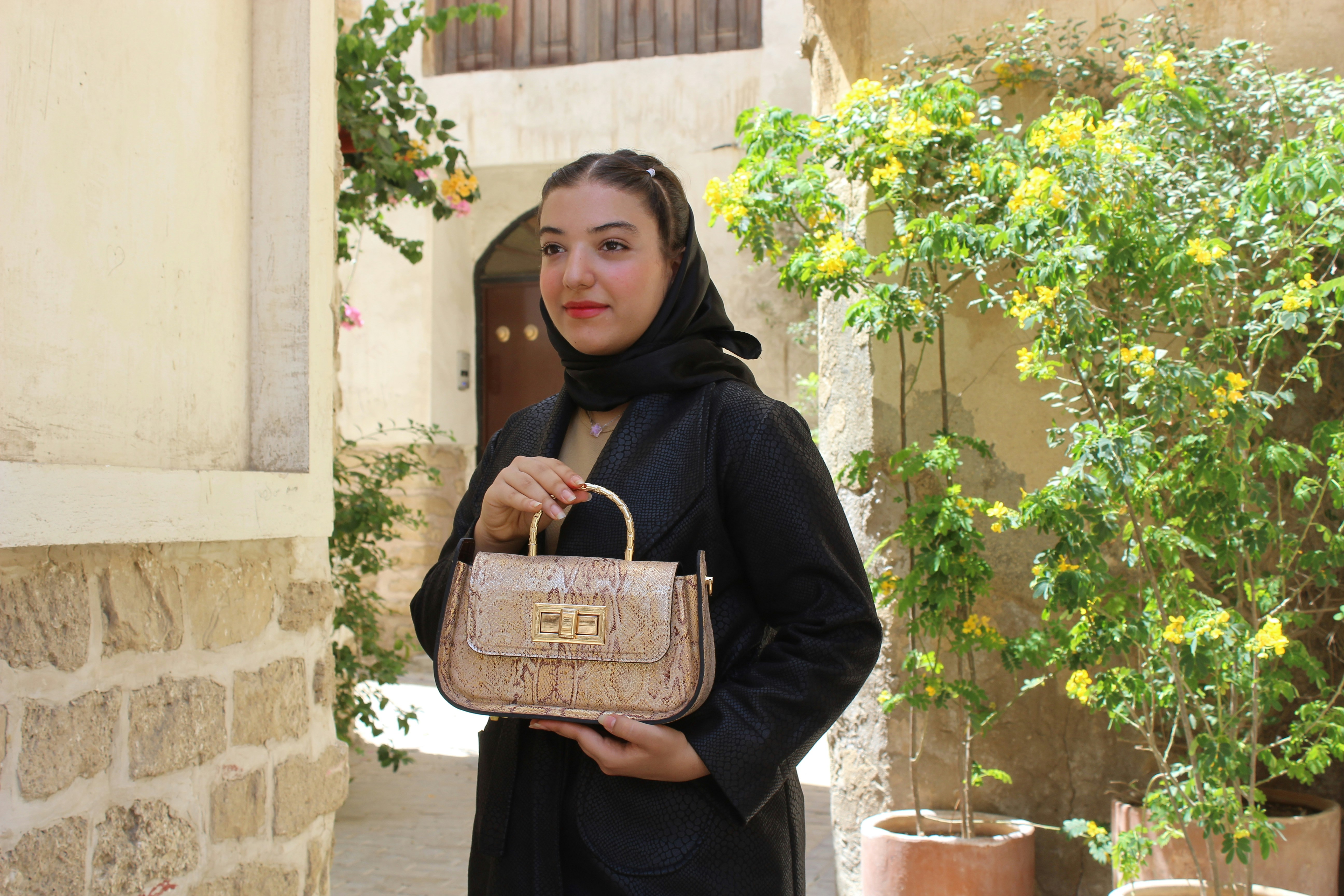 Young woman in black abaya holds a designer handbag.