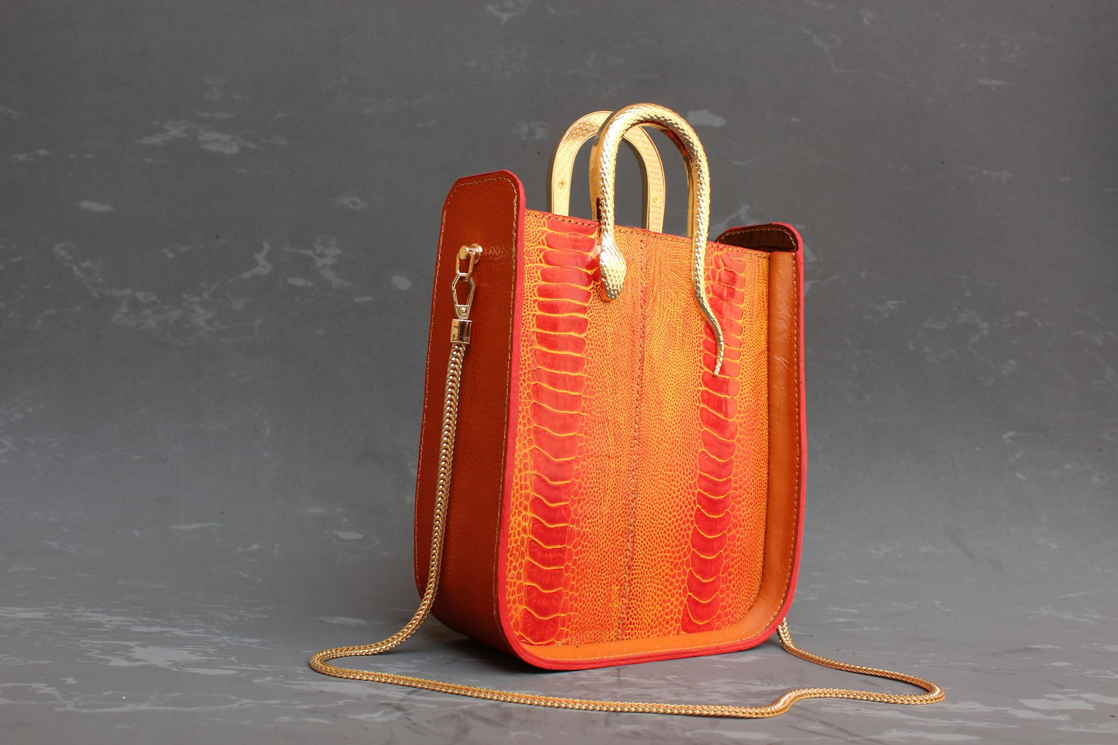 Un cabas en cuir rouge orangé texturé, anses dorées en forme de serpent