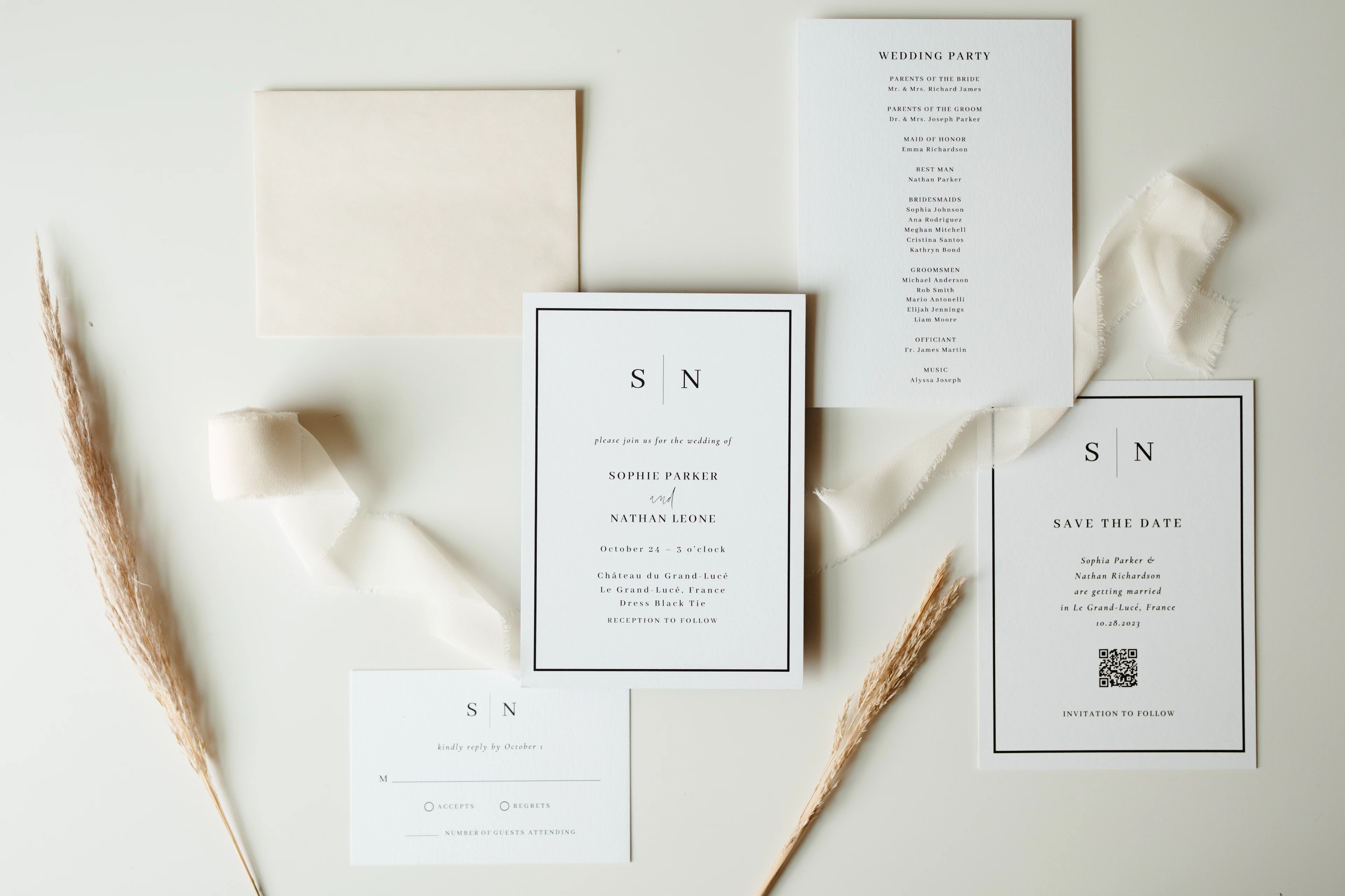 A minimalist invitation suite with silk ribbon and dried grasses on a white surface.
