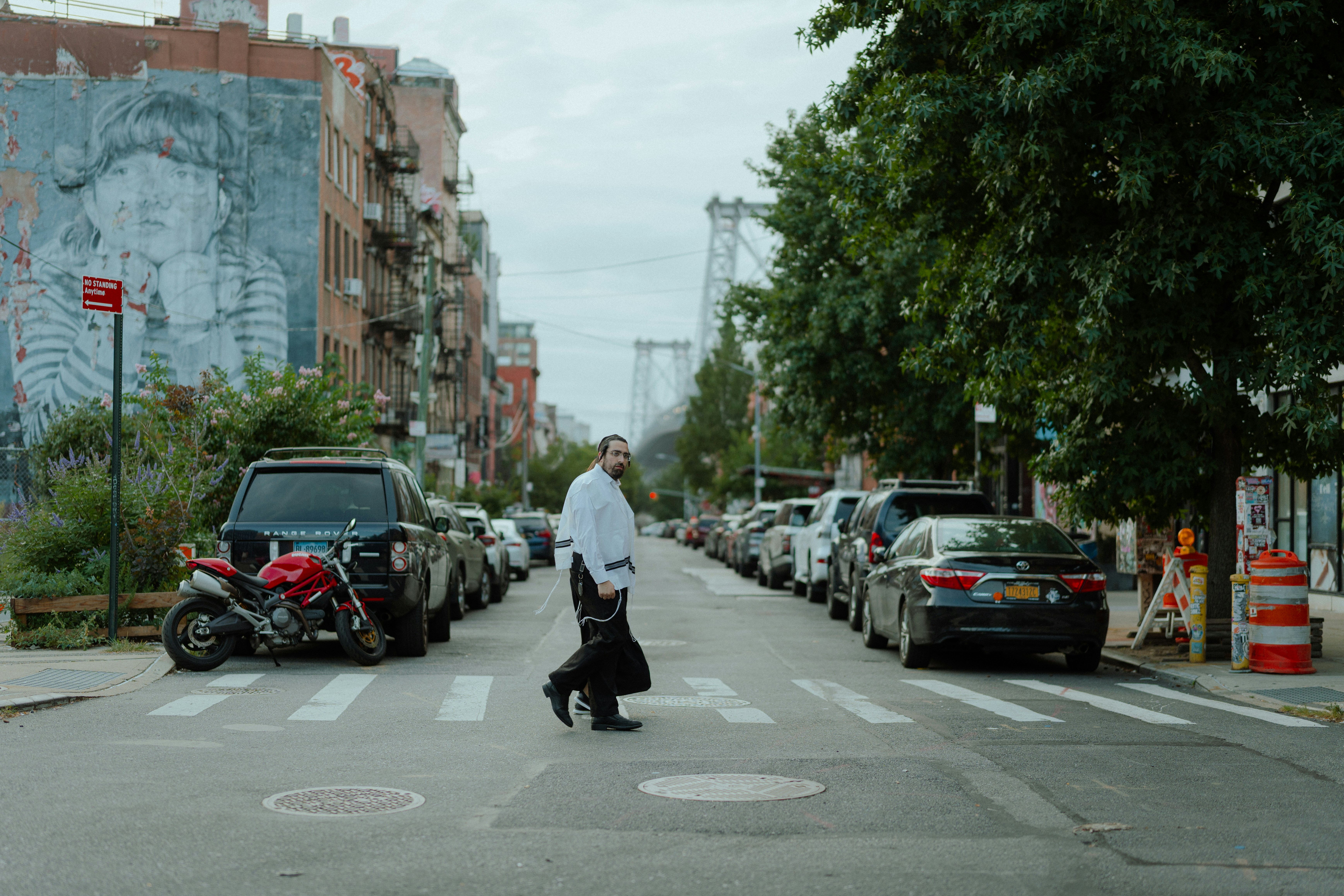 Man crosses a street lined with parked cars.