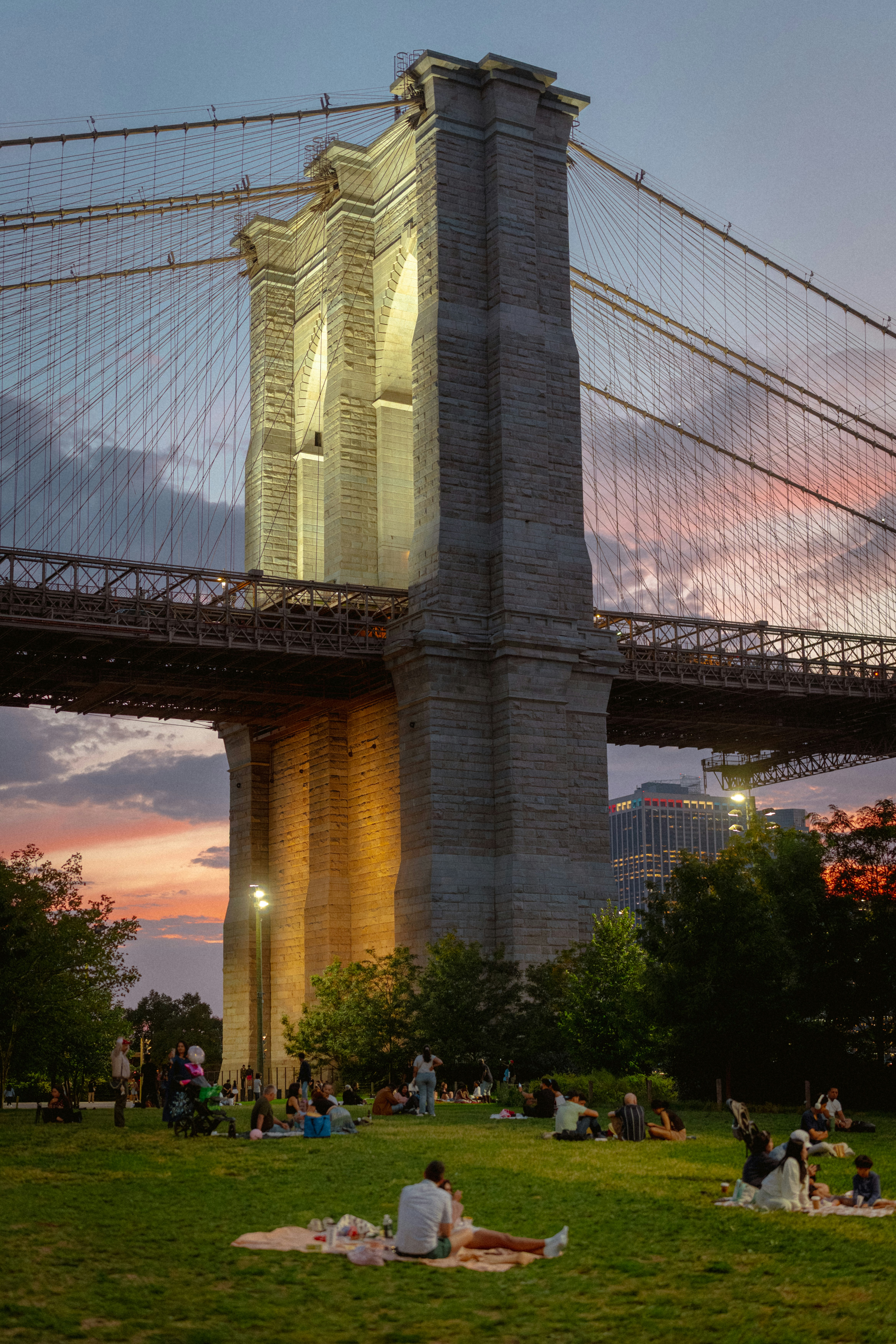 People enjoying a picnic under the brooklyn bridge at sunset.