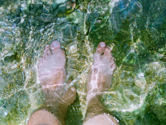 Feet submerged in clear, shallow water with stones.