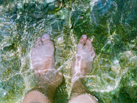 Feet submerged in clear, shallow water with stones.