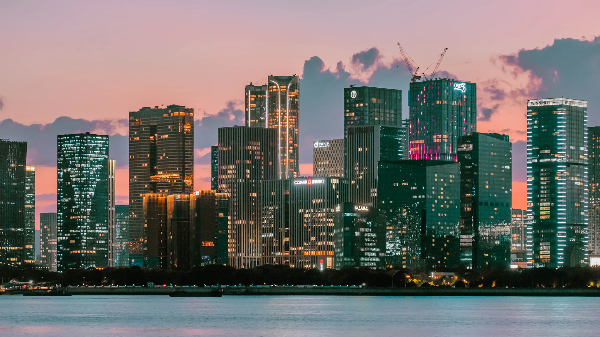City skyline at dusk with pastel sky and water.