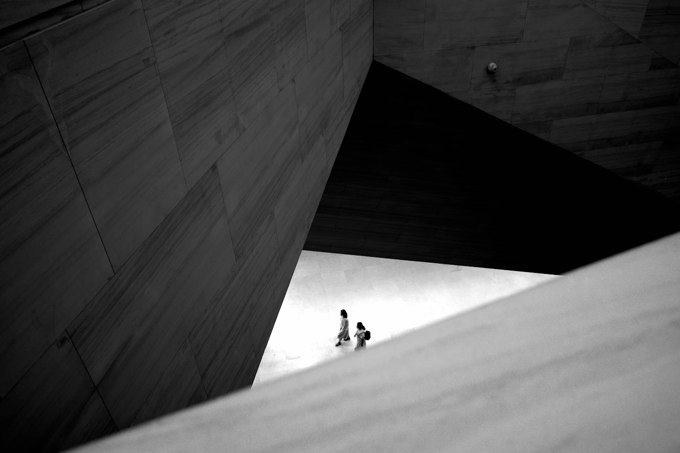 Two small figures stand inside a stark, angular concrete building washed with daylight