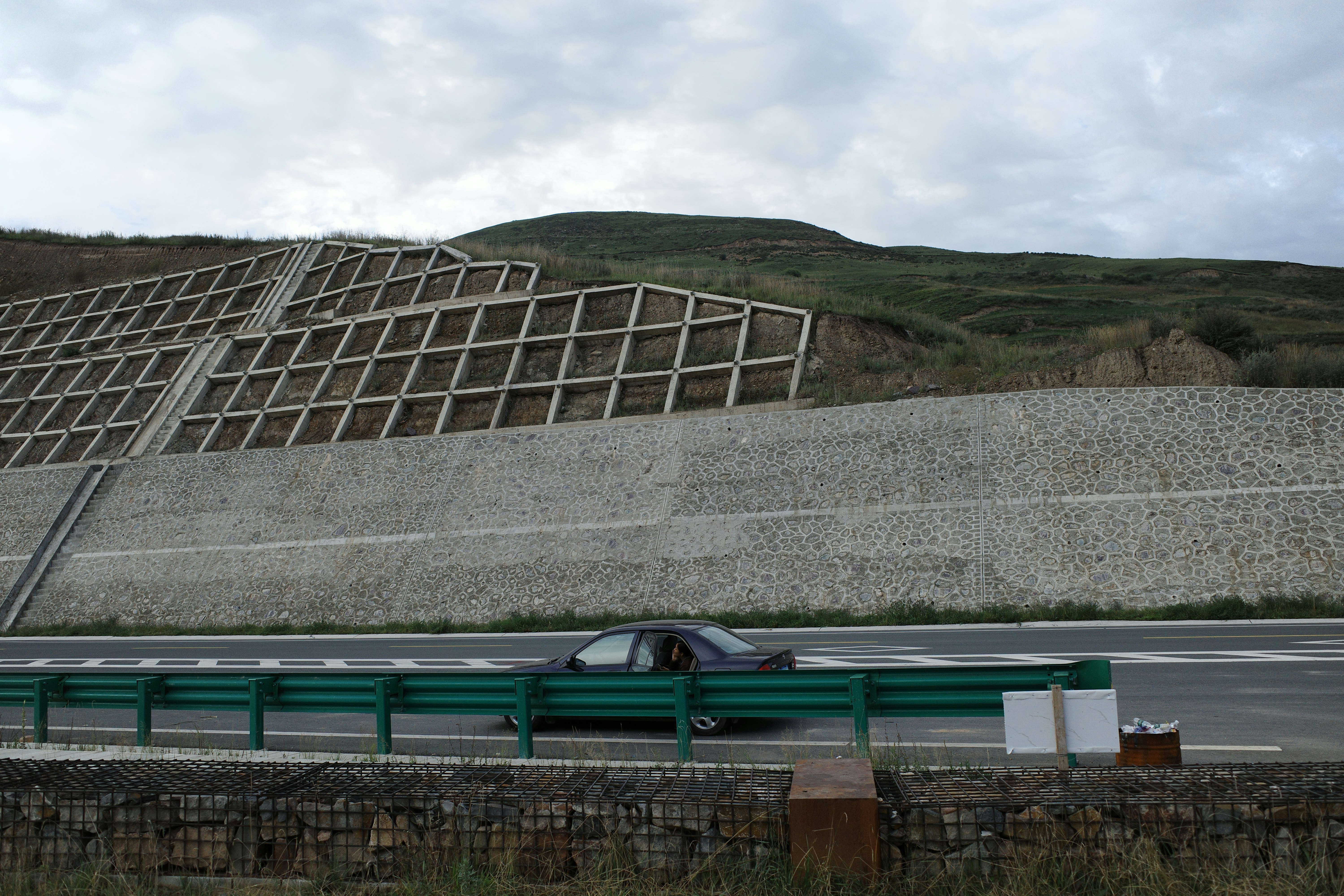 Car driving on highway next to retaining wall.