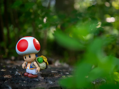Toad figurine with backpack in lush green forest.