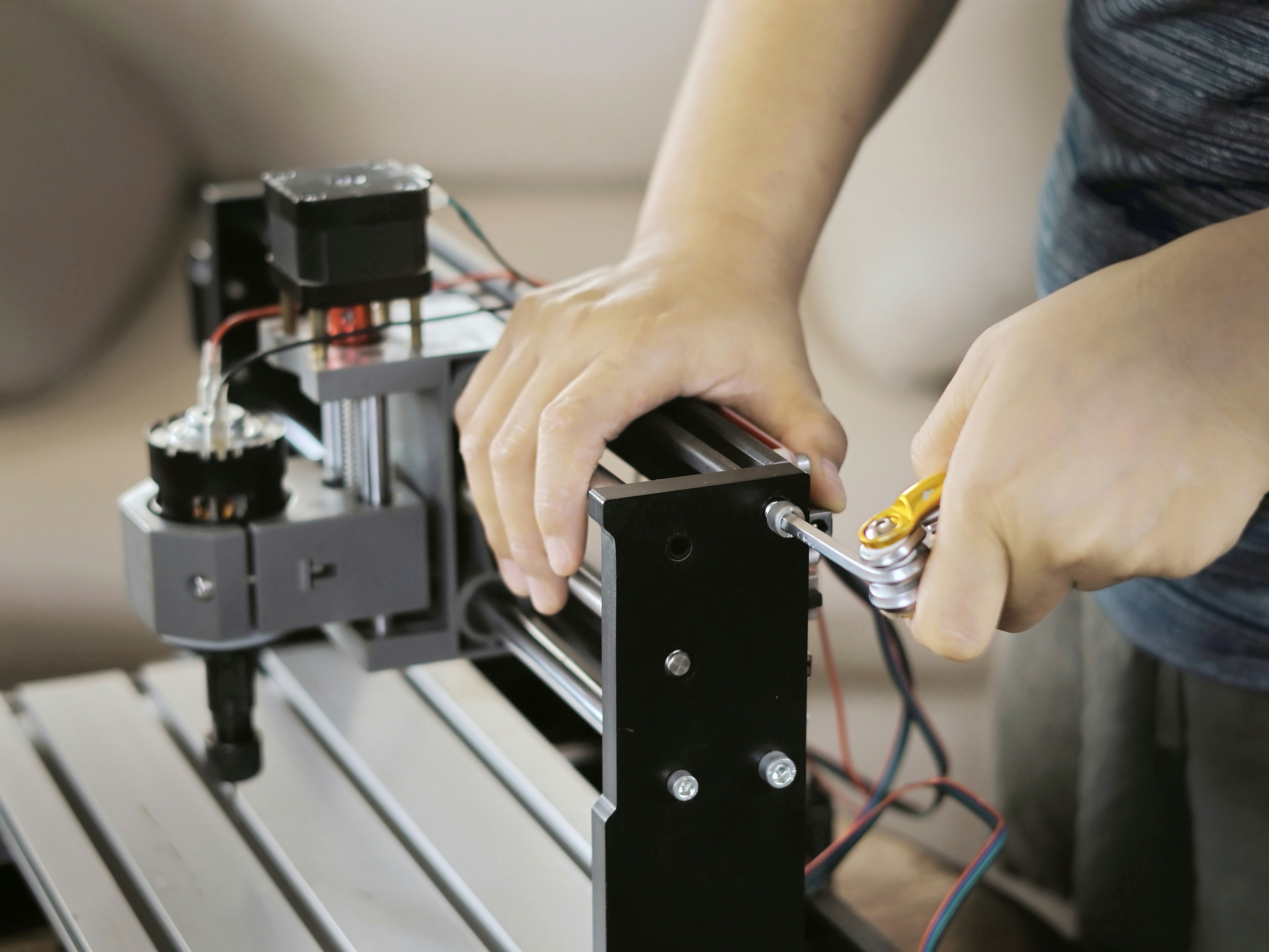 Hands use a yellow tool to tighten a machine screw.