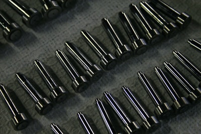 Rows of shiny metal components on a textured surface.