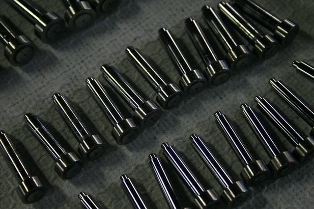 Rows of shiny metal components on a textured surface.
