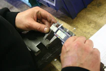 Hands using a digital caliper to measure metal part.