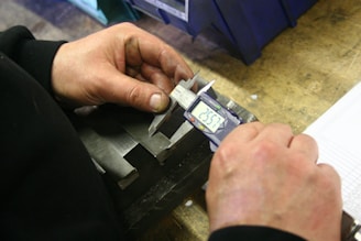 Hands using a digital caliper to measure metal part.