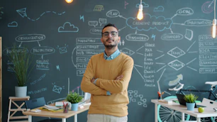 Man standing with arms crossed in front of chalkboard.