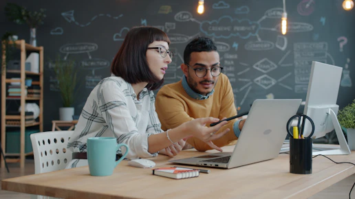 Two colleagues collaborating on a laptop at a desk.