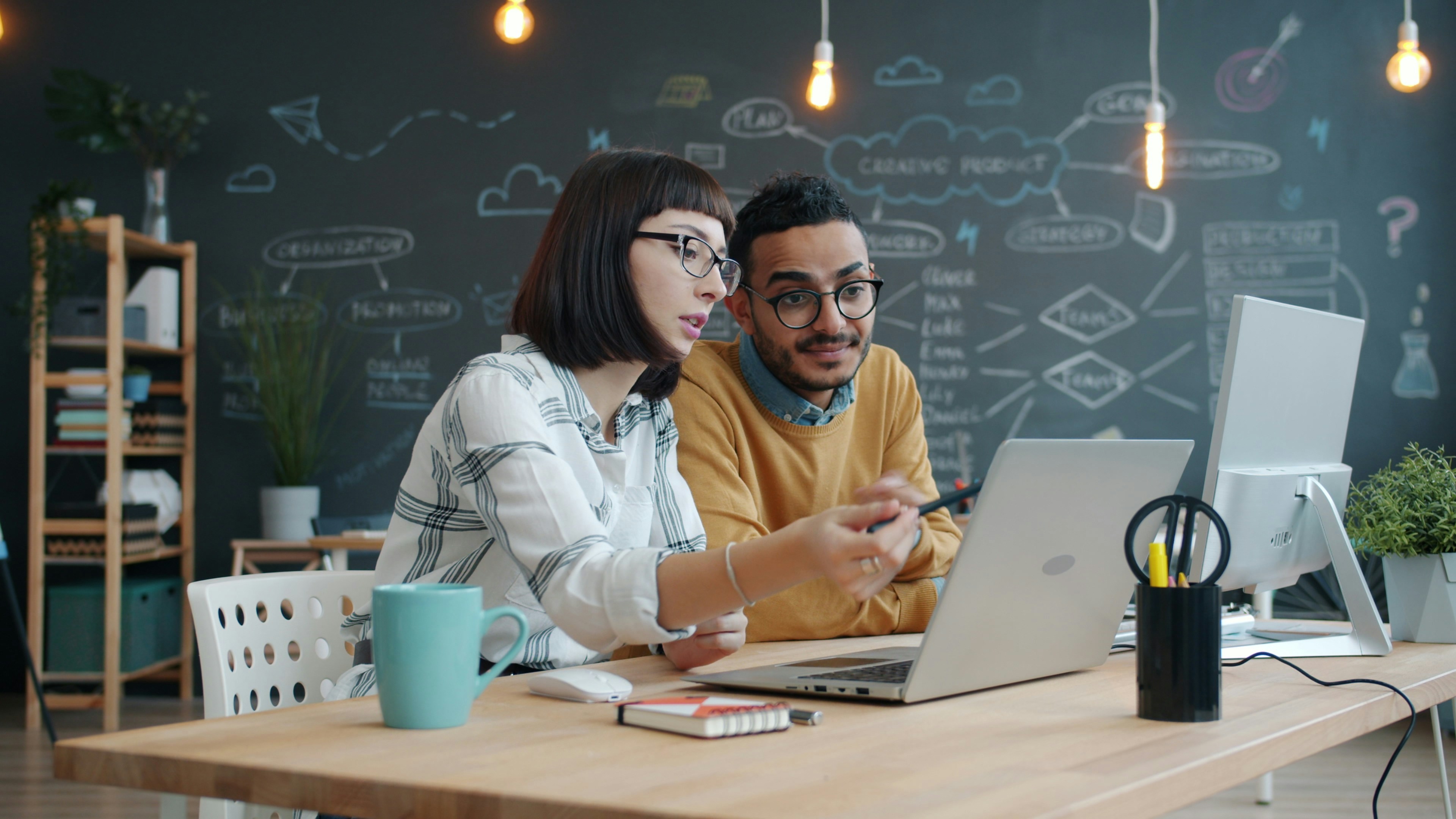 Two colleagues collaborating on a laptop at a desk.