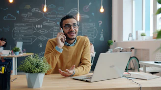 Man talking on phone at desk with laptop.