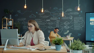 Woman working on computer in modern office with chalkboard.