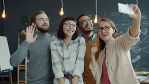 Four smiling friends taking a selfie in a modern office.