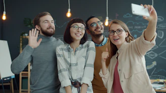 Four smiling friends taking a selfie in a modern office.