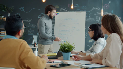 Colleagues gathered around a whiteboard in an office, discussing and pointing at notes during a working meeting
