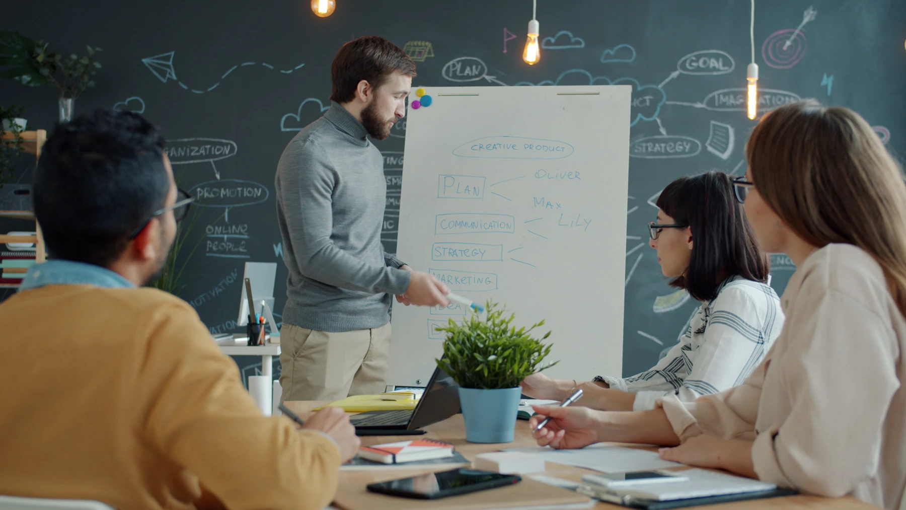 Colleagues gathered around a whiteboard in an office, discussing and pointing at notes during a working meeting