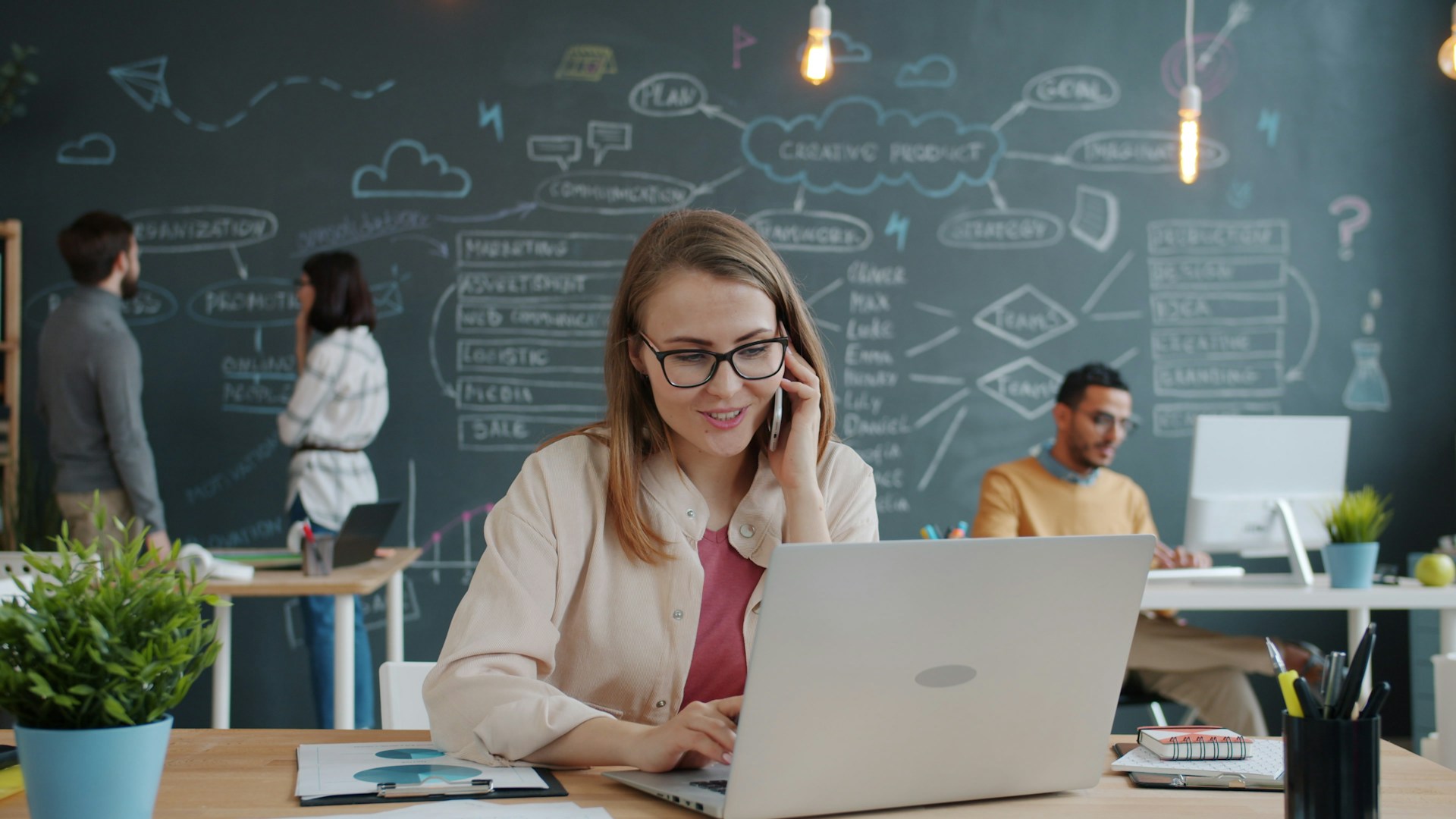 Woman on phone working on laptop in modern office.