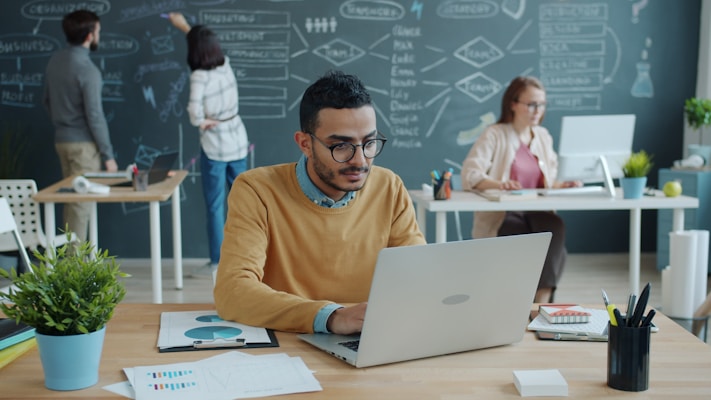 Man working on laptop in modern office with colleagues.