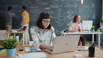 Woman working on laptop in modern office with team.