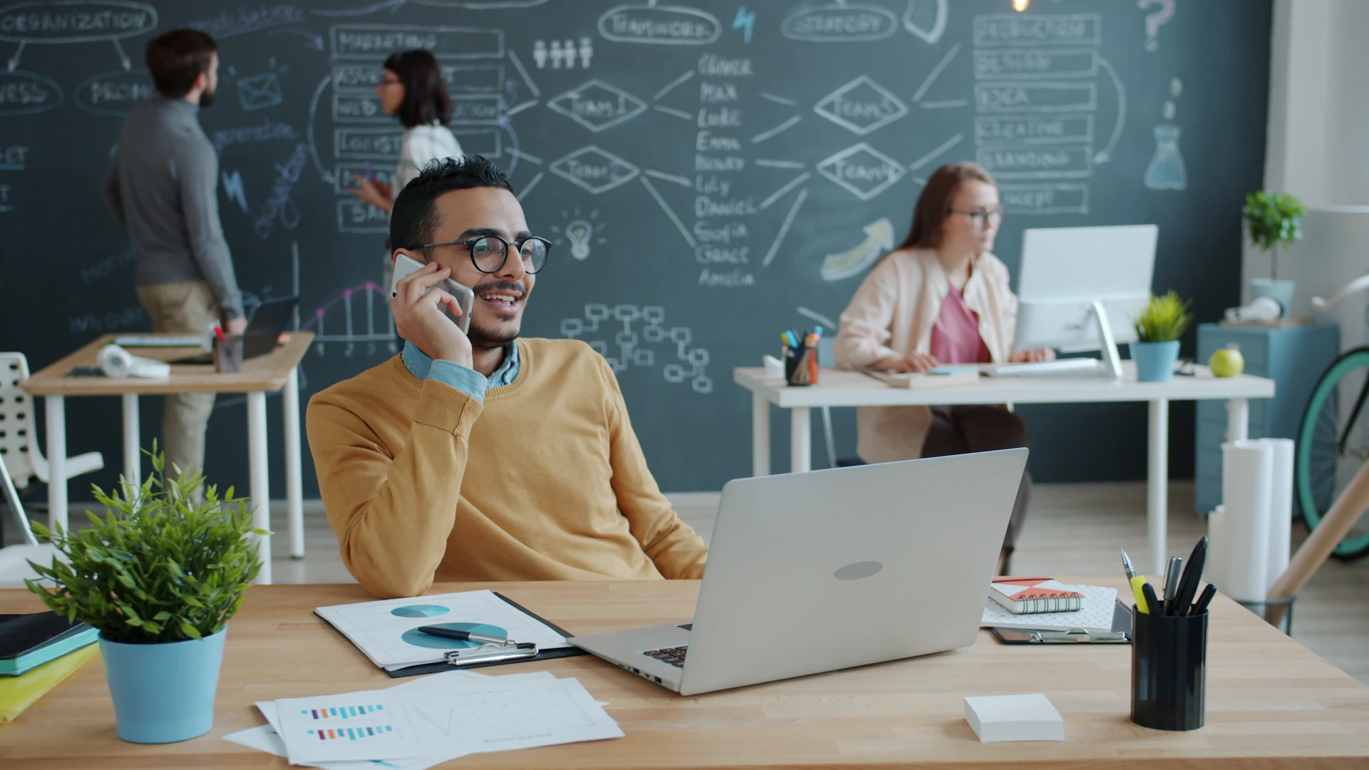 A professional taking a phone call at his desk in a modern open-plan office