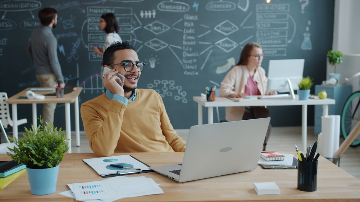 Man taking a phone call in a modern office with his team working behind him