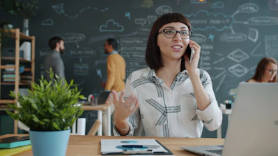 Woman talking on phone in modern office with chalkboard wall.