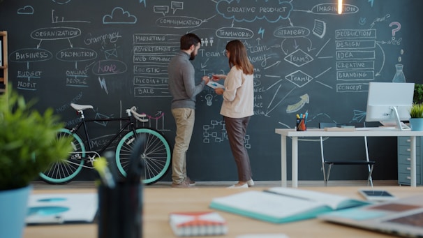 Two people discussing a diagram on a chalkboard wall.