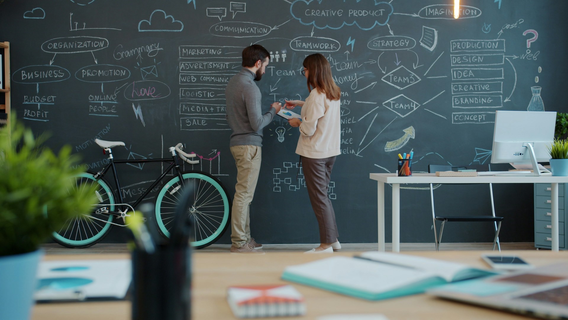 Two people discussing a diagram on a chalkboard wall.