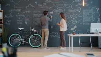 Two people drawing on a chalkboard wall.