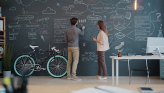 Two people drawing on a chalkboard wall.