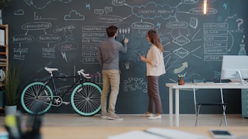 Two people drawing on a chalkboard wall.