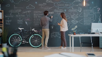 Two people drawing on a chalkboard wall.