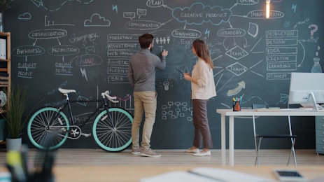 Two people drawing on a chalkboard wall.