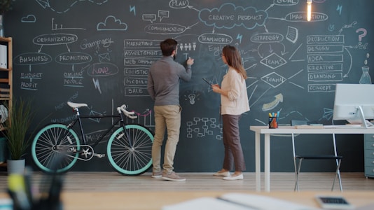 Two people drawing on a chalkboard wall.