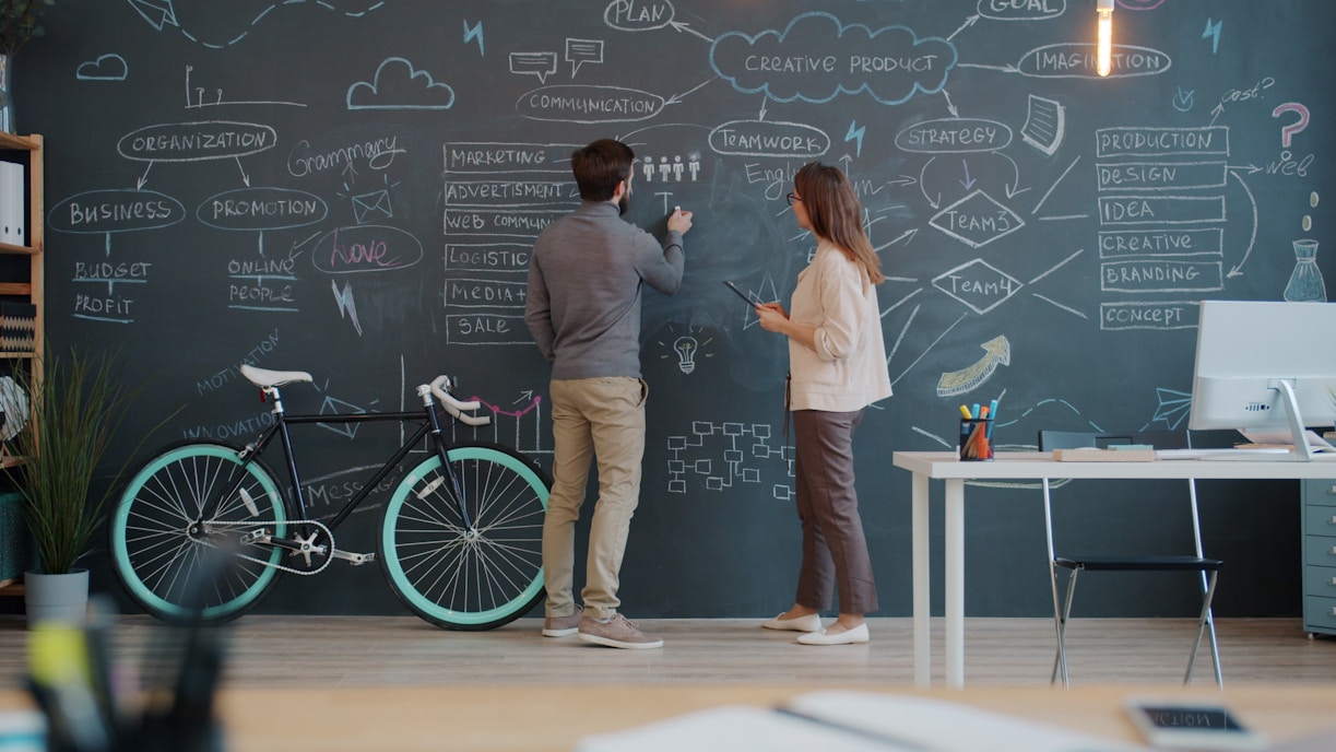 Two people drawing on a chalkboard wall.