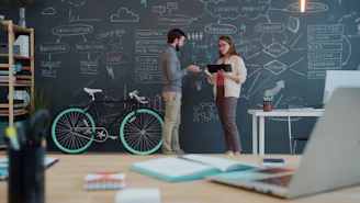 Two people discuss a plan on a chalkboard wall.