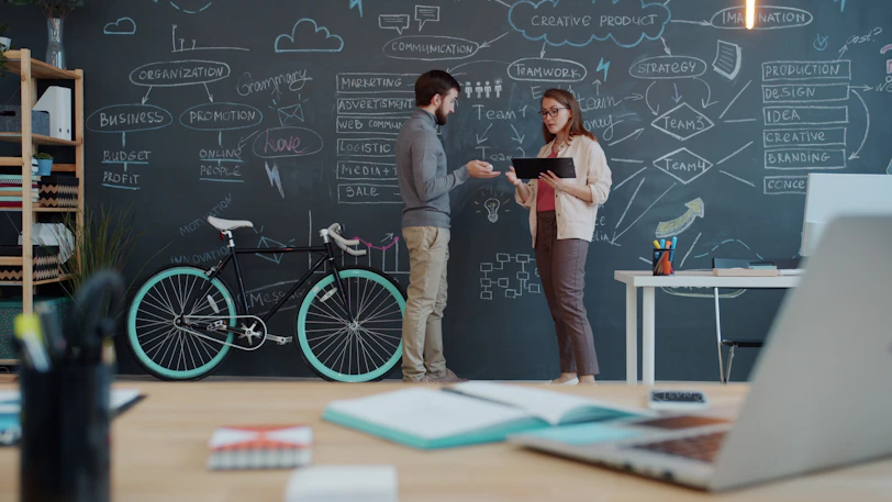 Two people discuss a plan on a chalkboard wall.