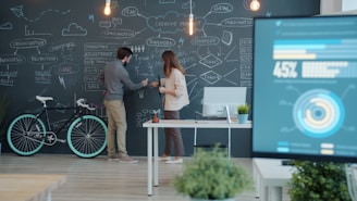 Two people collaborating on a chalkboard with a bicycle.