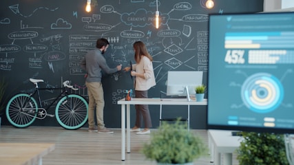 Two people collaborating on a chalkboard with a bicycle.