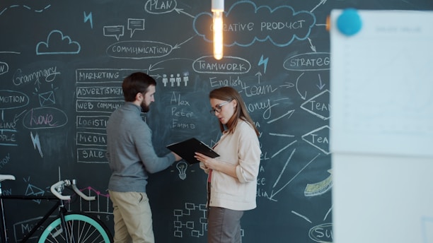 Two people discussing a business plan on chalkboard.