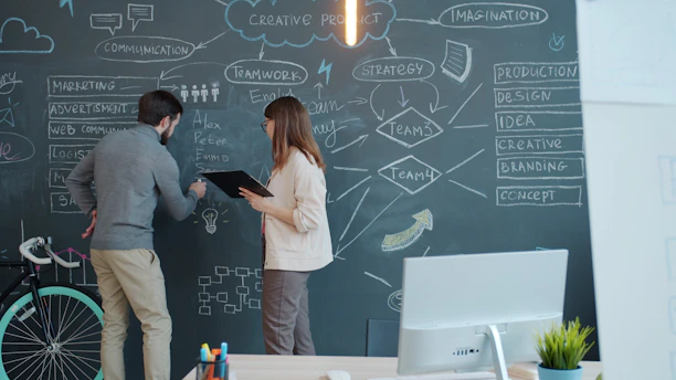 Two people brainstorming on a chalkboard wall.