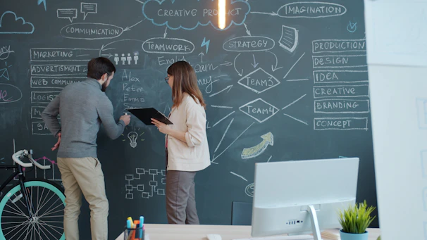 Two people brainstorming on a chalkboard wall.