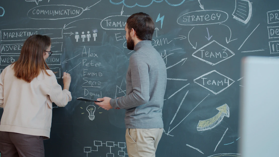 Two people planning on a chalkboard with diagrams.