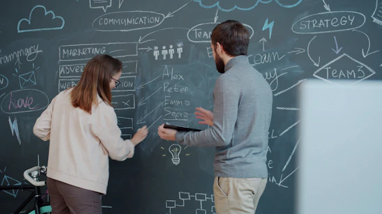 Two people collaborating on a chalkboard with diagrams.